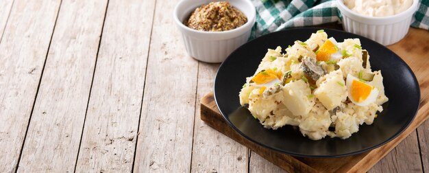 Ensalada de patatas con pepinillos, huevo y mostaza en mesa de madera