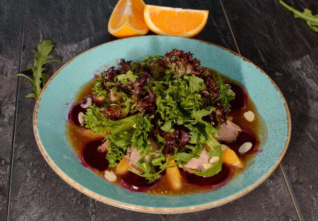 Ensalada con pato desmenuzado, almendras y naranja sobre un fondo de madera.