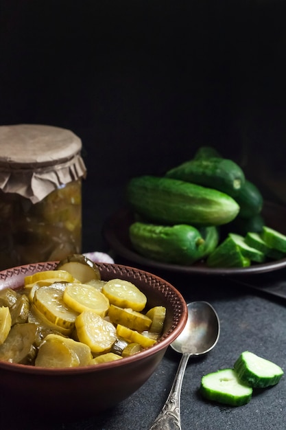 Ensalada de pepino encurtido en un recipiente y un tarro sobre fondo negro