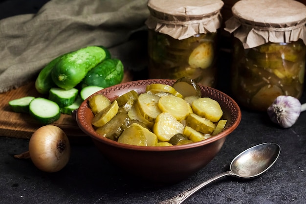 Ensalada de pepino en escabeche en un cuenco y frascos sobre fondo negro