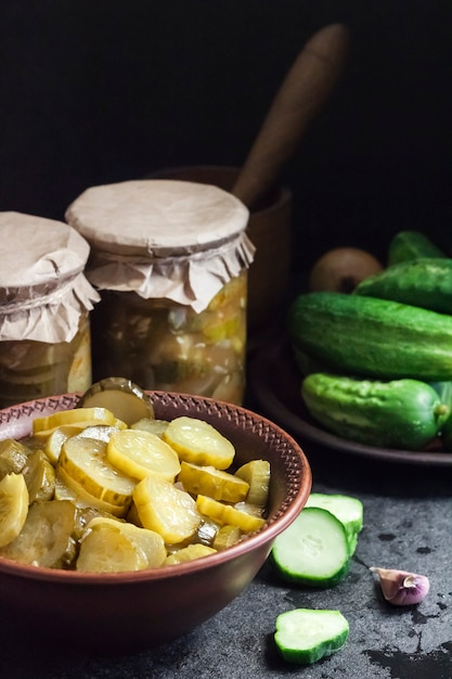 Ensalada de pepino en escabeche en un cuenco y frascos sobre fondo negro