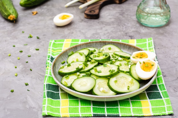 Ensalada de pepino fresco, huevos de gallina hervida y cebolla verde en un plato sobre la mesa