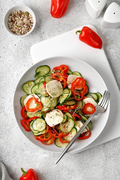 Ensalada de pepinos en rodajas con pimientos dulces queso feta micro verduras en plato blanco con tenedor sobre fondo gris