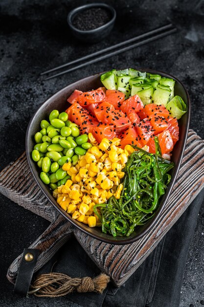 Ensalada de pescado crudo hawaiano Poke bowl con salmón Pepino Edamame y arroz Fondo negro Vista superior