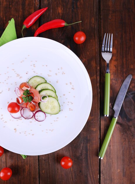 Ensalada de pescado fresco con verduras en un plato en una mesa de madera de primer plano