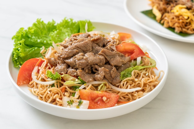 Ensalada picante de fideos instantáneos con carne de cerdo en la placa blanca - estilo de comida asiática