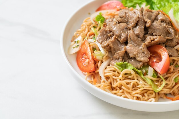 Ensalada picante de fideos instantáneos con carne de cerdo en la placa blanca - estilo de comida asiática