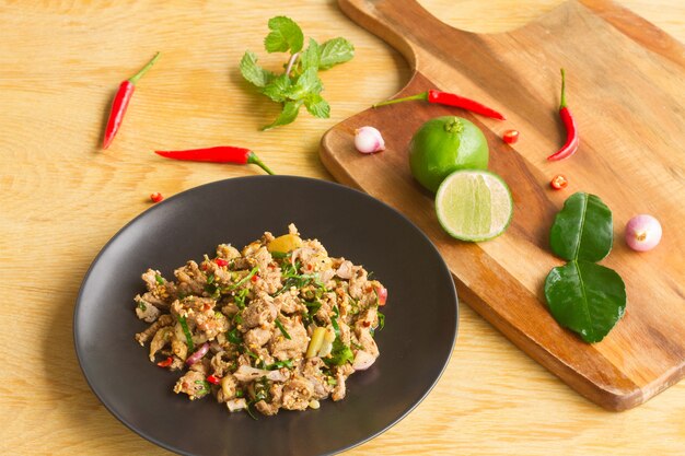 Ensalada picante de pato picada en un plato negro sobre una mesa de madera