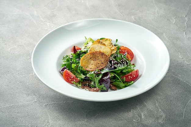 Ensalada con picatostes de tomate y ternera en un plato blanco Fondo de hormigón