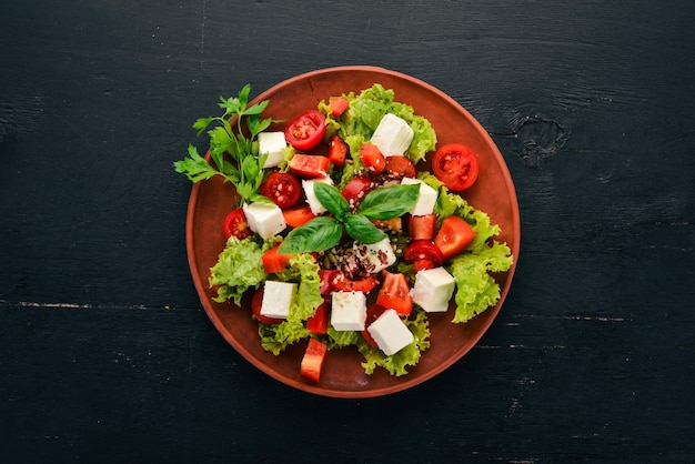 Ensalada en un plato Queso feta Tomates cherry Pimentón Lechuga Comida saludable En la mesa de madera negra Mesa Vista superior Espacio libre para texto