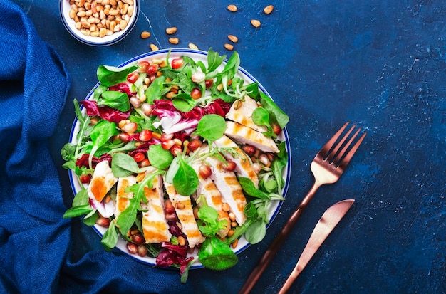 Ensalada con pollo a la parrilla, espinacas, rúcula, nueces de cedro y semillas de granada. Comida saludable y concepto de alimentación. Vista superior. Fondo azul.