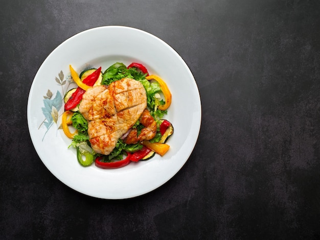 Foto ensalada de pollo y verduras asadas con fondo negro y plato blanco