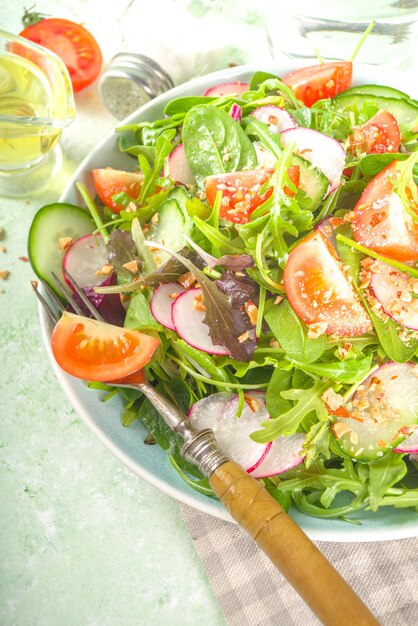 Ensalada de primavera colorida fresca - con tomates, aguacate, nueces, pepino, rábano de primavera, en el espacio de copia de fondo verde claro. Concepto de comida sana de dieta de primavera