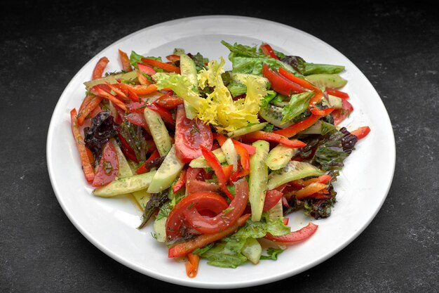 Ensalada de primavera de verduras frescas, pepinos, tomates, lechuga, pimiento en un plato blanco, sobre un fondo oscuro