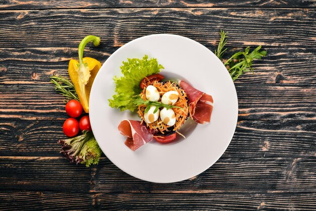 Ensalada con prosciutto, huevos de codorniz, ciruelas pasas y verduras frescas en el plato Sobre un fondo de madera Vista superior Espacio libre para texto