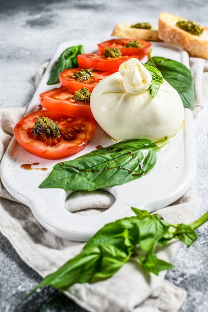 Ensalada de queso burrata que incluye tomate en rodajas, hojas de albahaca con pesto. Fondo gris Vista superior