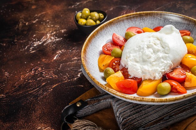 Ensalada de queso burrata y tomates servida en un plato rústico. fondo oscuro Vista superior. Copie el espacio.