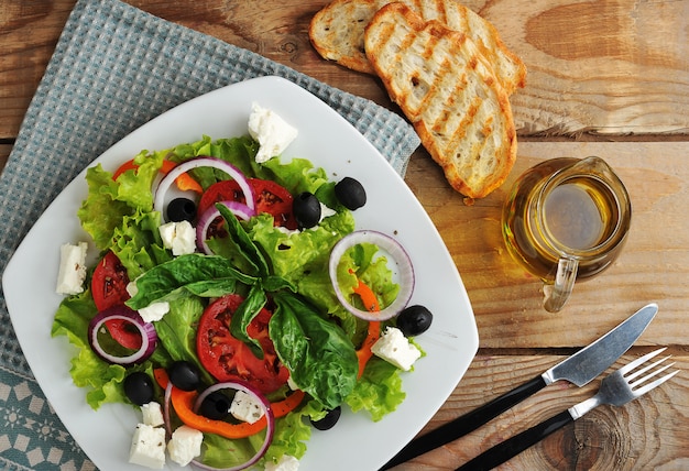 Ensalada con queso feta, aceitunas, tomates y lechuga y albahaca sobre superficie de madera