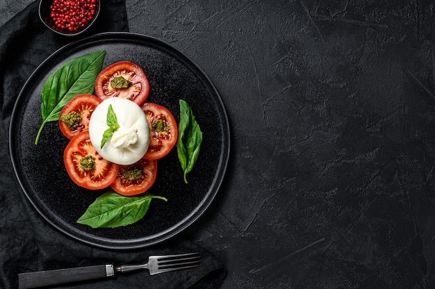 Ensalada de queso y tomate burrata servido en plato negro. Fondo oscuro Vista superior. Espacio para texto