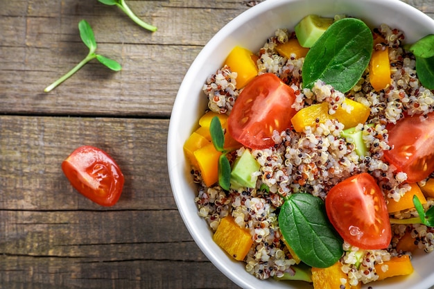 Foto ensalada de quinua con tomate, batata y espinacas sobre fondo de madera. concepto de comida vegana. vista superior.