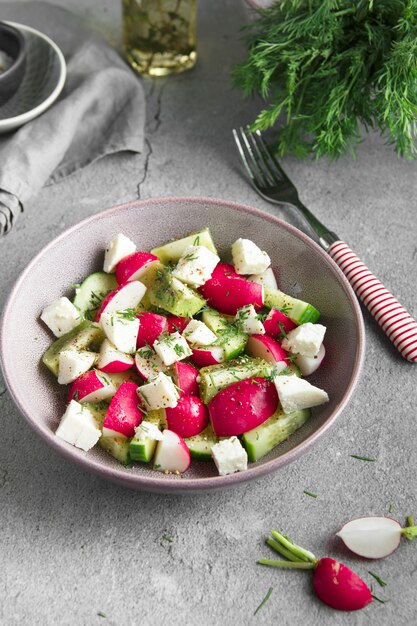 Ensalada de rábano, pepino, kiwi, queso y eneldo en un recipiente sobre fondo de hormigón gris grunge.