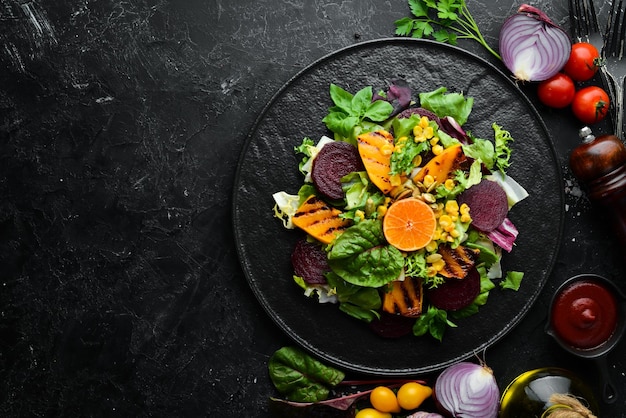 Ensalada de remolacha, calabaza, maíz y lechuga en un plato negro sobre un fondo negro Vista superior Espacio libre para el texto