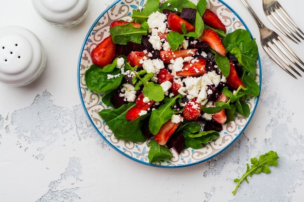 Ensalada de remolacha, fresas, queso feta y rúcula en placa de cerámica sobre la superficie de la mesa de hormigón antiguo. Vista superior.