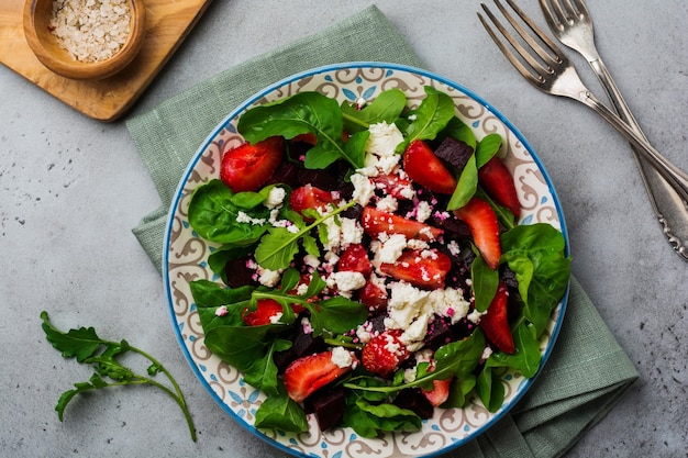 Ensalada de remolacha, fresas, queso feta y rúcula en placa de cerámica en la vieja mesa de hormigón.