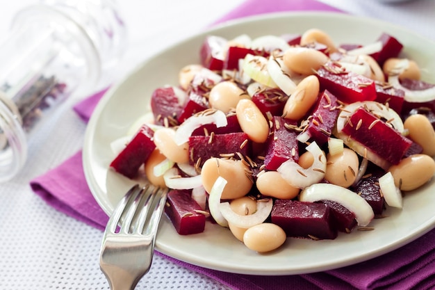 Ensalada de remolacha con frijoles blancos, pepinillos y cebolla en una placa blanca con un tenedor