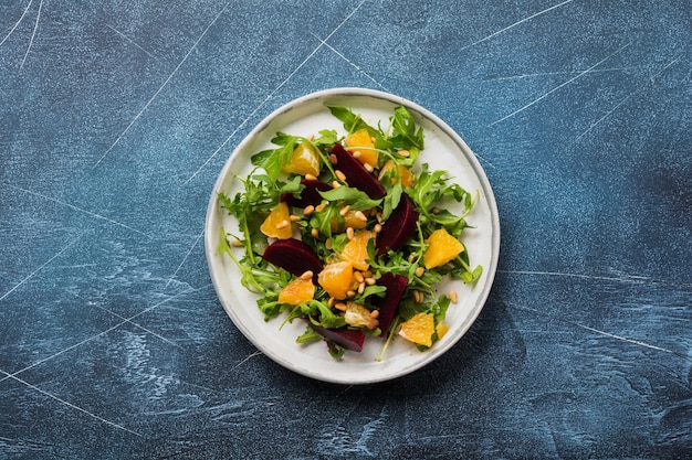 Ensalada de remolacha, naranja, piñones, aceite de oliva, queso feta y rúcula en placa de cerámica en la vieja mesa de hormigón