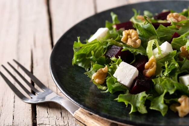 Ensalada de remolacha con queso feta, lechuga y nueces sobre mesa de madera rústica