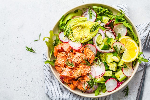 Ensalada roja cocida de los pescados con el aguacate, el pepino, el rábano y el arugula en la placa blanca, visión superior.