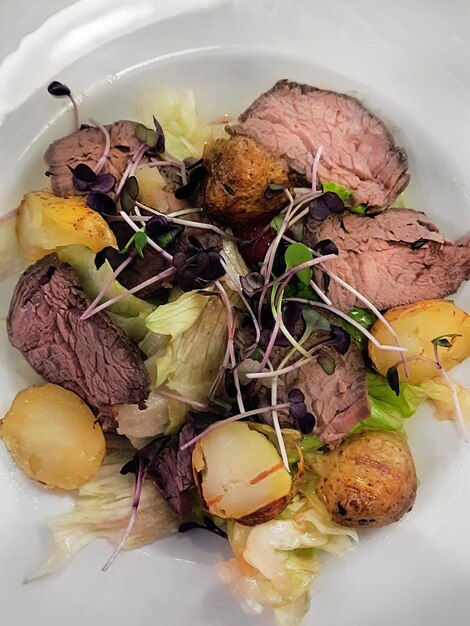 Ensalada con rosbif y patatas fritas en primer plano de plato blanco