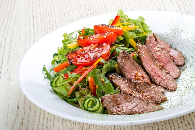 Ensalada con rosbif y tomates secos sobre fondo blanco.