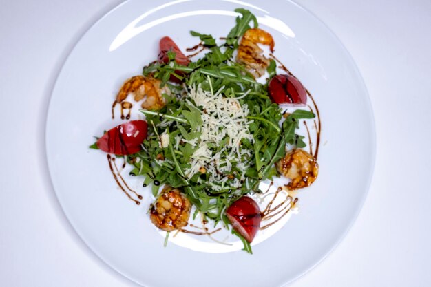 Ensalada con rúcula y camarones a la parrilla en un plato blanco y vista superior de fondo blanco mediterráneo