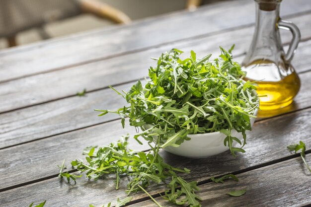 Ensalada de rúcula fresca con aceite de oliva en un plato blanco sobre la mesa de madera.