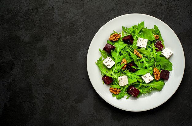 Ensalada de rúcula, queso, remolacha, nuez, sobre un fondo de pizarra, piedra u hormigón.