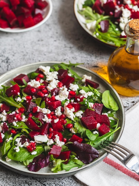 Ensalada de rúcula, remolacha y queso con granada y aderezo en un plato sobre una mesa de cocina de piedra gris, lugar de fondo para la vista superior del texto