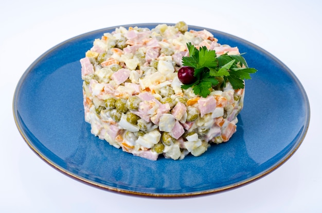 Ensalada rusa de verduras con guisantes y mayonesa en placa azul. Foto de estudio