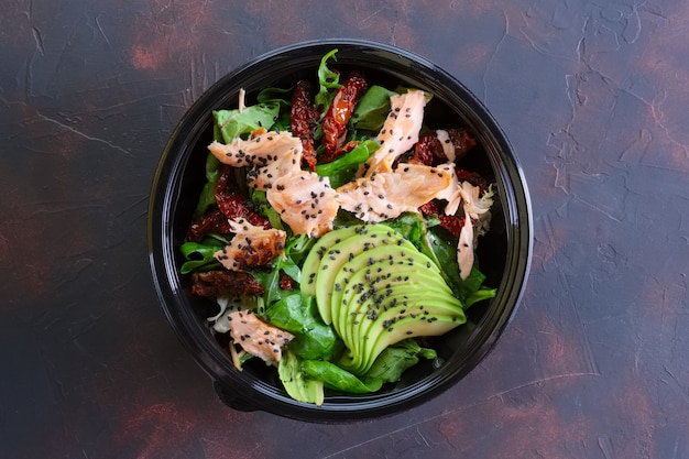 Ensalada con salmón, aguacate y tomates secos en envases para llevar.