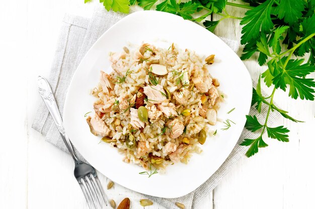 Ensalada de salmón ahumado, arroz, semillas de girasol y calabaza, almendras, condimentado con miel y aceite de oliva en un plato sobre una toalla, perejil y tenedor sobre fondo de tablero de madera desde arriba