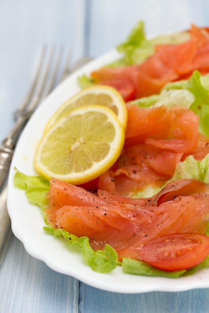 Ensalada con salmón en plato blanco sobre madera azul