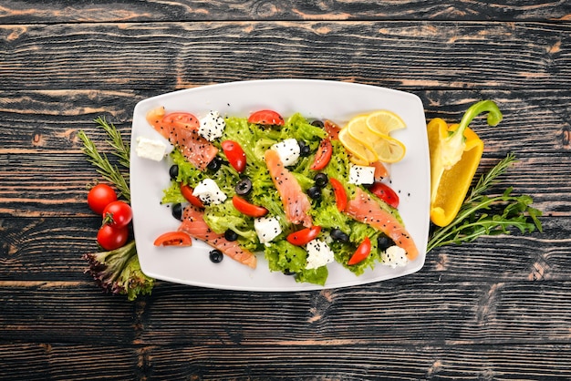 Ensalada de salmón, queso feta, hojas de ensalada y verduras frescas en el plato Sobre un fondo de madera Vista superior Espacio libre para texto