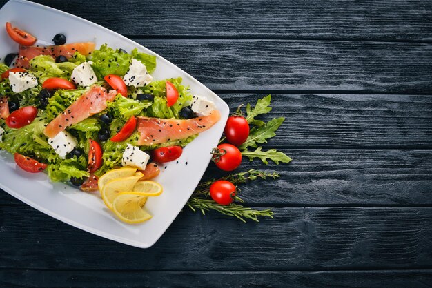 Ensalada de salmón, queso feta, hojas de ensalada y verduras frescas en el plato Sobre un fondo de madera Vista superior Espacio libre para texto