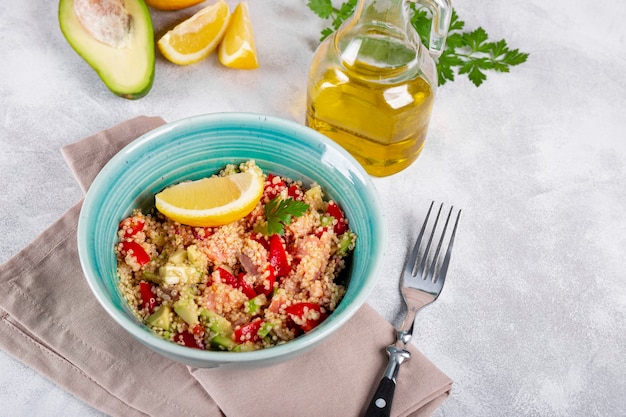 Ensalada de salmón con tomate, aguacate y quinua en un recipiente azul sobre una mesa gris claro, un plato de nutrición equilibrada.