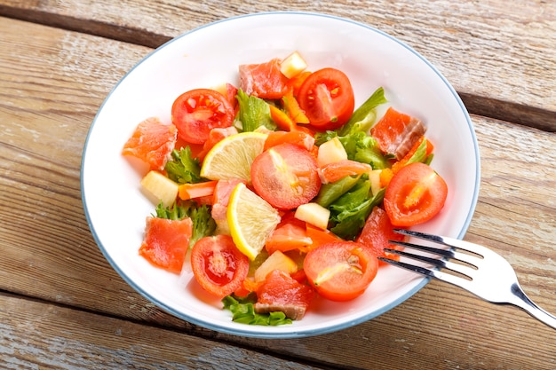 Foto ensalada de salmón y tomates cherry y ensalada verde en un plato sobre una mesa de madera con un tenedor.