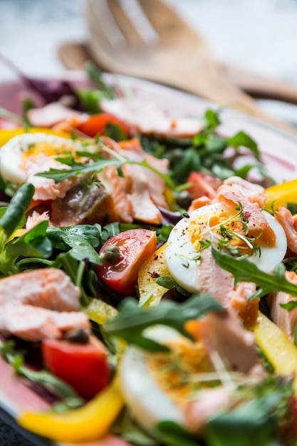 Ensalada con salmón y verdura en placa rosa sobre fondo retro periódico