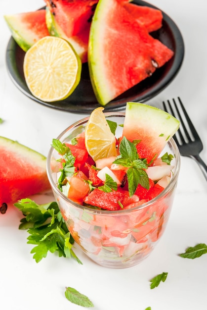 Ensalada de salsa de verduras con sandía, tomates, cebollas, verduras, lima en porciones de vidrio