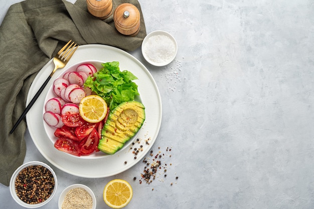 Ensalada saludable con aguacate, tomate, rábano y lechuga sobre un fondo gris claro.