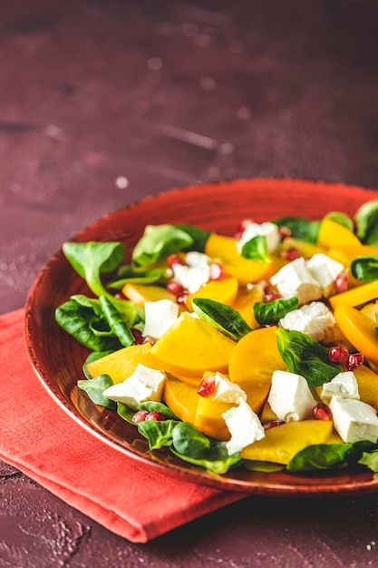 Ensalada saludable con caqui doucette lambslettuce cornsalad ensalada de campo y queso feta en un plato rojo sobre un fondo rojo superalimentos vitamina ensalada de caqui